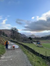 A wide gravel path through a rural valley, with stone walls, open fields, and distant hills under a large sky.