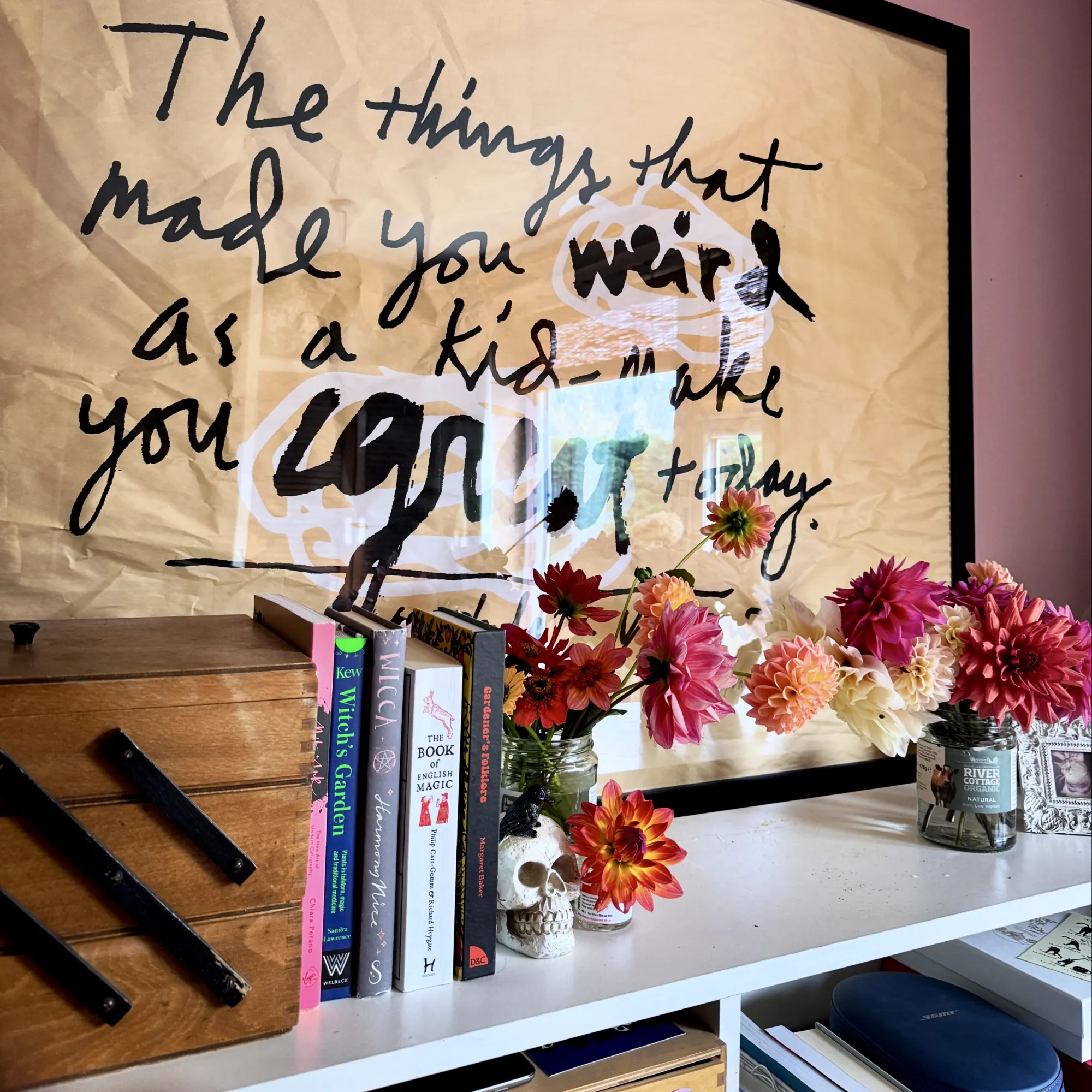 The poster behind my desk reads "The things that made your weird as a kid make you great today" on the bookshelf below are books about witches and gardening and two jars of dahlias from my allotment